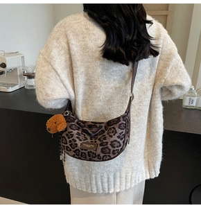 Detail of leopard print crescent bag with leather strap and plush bear charm on a model