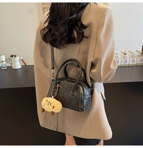 Detail der schwarzen Kissen-Tasche aus genarbtem Leder mit weißer Naht und Anhänger