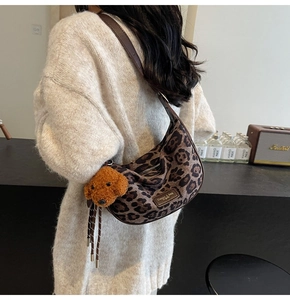 Detailed view of leopard print crescent bag with leather strap and plush dog charm accessory
