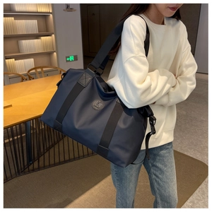 Detail view of navy blue waterproof oxford travel bag worn by a model in a cozy bookstore