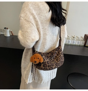 Close-up of leopard print crescent bag with leather strap and plush dog charm