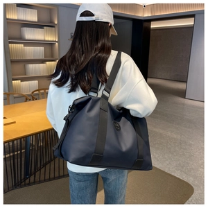 Navy blue oxford travel bag shown by model in minimalist room to display large capacity size