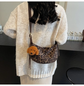 Detailed shot of leopard print crescent bag with a cute plush dog charm on the strap