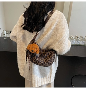 Detailed shot of leopard print crescent bag with brown strap and dog pendant accessory