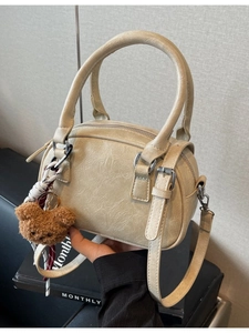 Minimalist beige Boston pillow bag with plush bear charm and adjustable shoulder strap