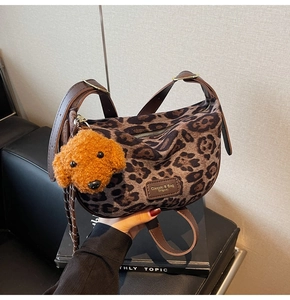 Detail of leopard print hobo bag featuring brown leather strap and plush dog charm