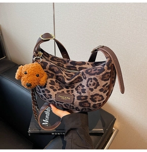 Detail of leopard print hobo bag with brown strap and plush dog charm on a sofa