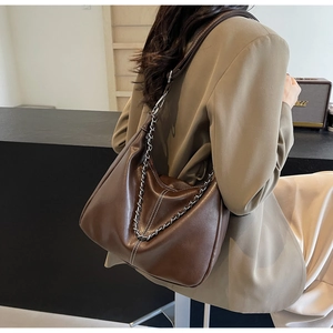 Detailansicht der braunen Ledertasche mit Metallkette und modischen weißen Nähten