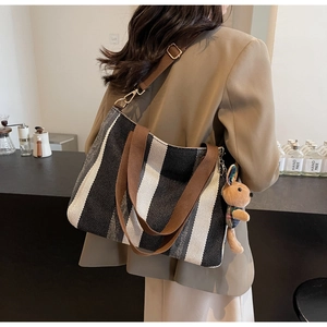 Detail of striped woven tote bag featuring brown handles and a cute rabbit pendant