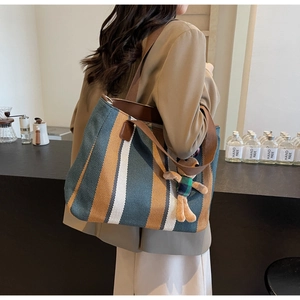 Detailed shot of striped canvas tote bag with brown leather trim and a small teddy bear charm