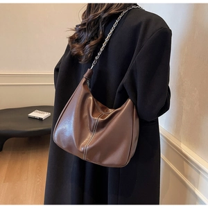 Detail einer braunen Hobo-Tasche mit weißen Kontrastnähten und silbernem Kettenriemen