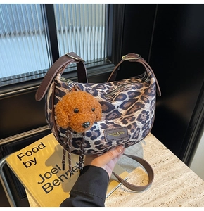 Detail of leopard print crescent bag with leather trim and plush dog charm accessory