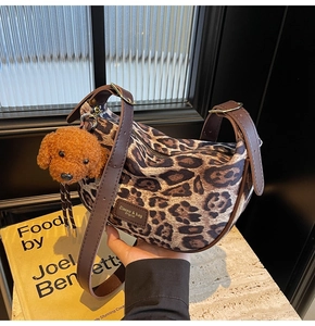 Detail of leopard print hobo bag with adjustable brown strap and plush poodle charm