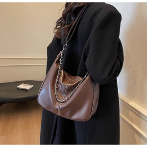 Detail einer dunkelbraunen Ledertasche mit silberner Kette und weißen Steppnähten