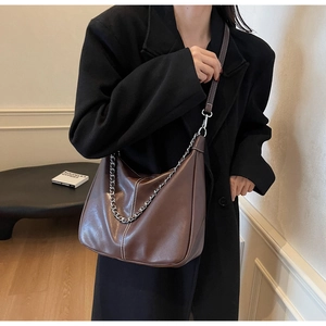Detailansicht einer braunen Hobo-Tasche aus Leder mit Kette und schwarzem Mantel.