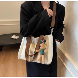 Close-up of a striped canvas tote bag with a cute plush rabbit charm on a model