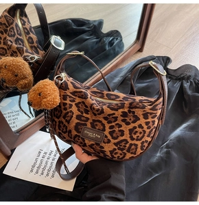 Detail of leopard print crescent bag texture with plush pendant and brand label