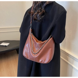 Detail der karamellbraunen Hobo-Bag mit weißen Nähten und silberner Kette am Modell
