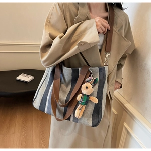 Detail of striped canvas tote bag with brown handles and a cute rabbit plush charm