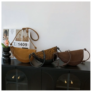 Three minimalist half-moon crossbody bags in yellow, leopard, and brown on a vintage cabinet