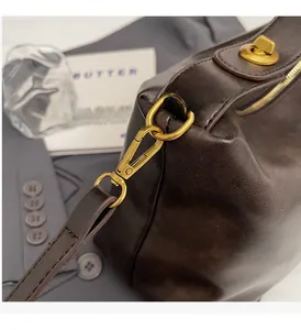 Detail of high-gloss dark brown leather bag with shiny golden hardware and metal lobster clasp