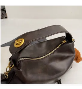 Detailed shot of dark brown PU leather handbag with gold twist lock and plush pompom charm