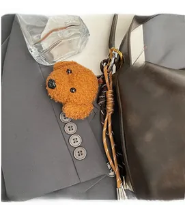 Detail of cute brown teddy bear plush charm with woven rope attached to a leather bag