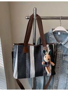 Vertical striped woven tote bag in black, grey, white with brown straps and plush rabbit charm