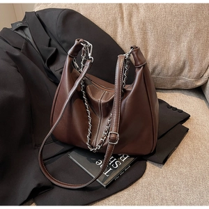 Detail einer braunen Ledertasche mit weißen Kontrastnähten und silberner Kettenverzierung