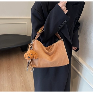 Close-up of brown suede hobo tote bag featuring a leather strap and plush dog charm