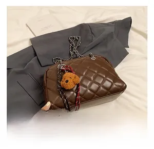 Detail of brown quilted pillow bag with chain strap and teddy bear charm accessory