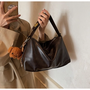 Macro shot of dark brown polished leather tote bag with gold metal buckle and plush bear charm