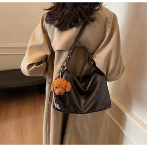 Detail of dark brown leather tote bag with a cute plush dog pendant on a beige coat