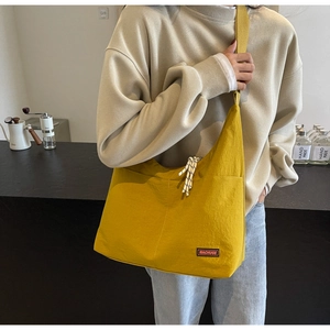 Detail der gelben Canvas-Hobo-Tasche mit MACHUGE-Markenlabel und gewebtem Umhängegurt