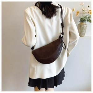 Detail of dark brown suede half-moon bag with knotted shoulder strap on white blazer