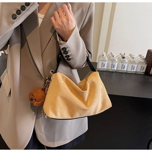 Detail of yellow suede hobo bag with black leather handle and cute brown bear charm