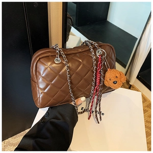 Detail of brown quilted chain bag with teddy bear charm and woven rope accessory