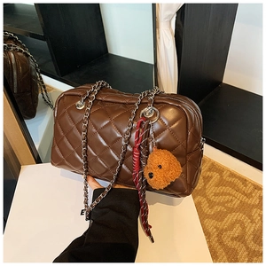 Detail of a brown quilted pillow bag featuring a silver chain and a plush teddy charm