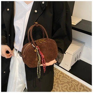 Détail d'un sac bowling en daim marron avec ferrures dorées et breloques de style