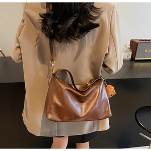 Detail view of brown matte leather shoulder bag with plush bear charm and adjustable strap