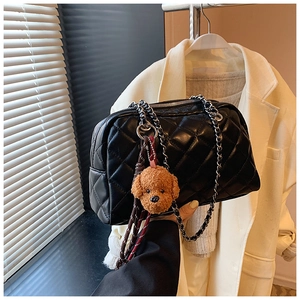 Detail of black quilted shoulder bag with chain strap and a brown plush teddy bear charm