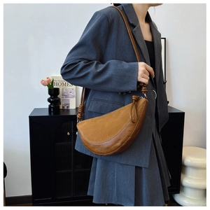 Detail of a brown two-tone crossbody bag with woven knot strap on a grey suit model