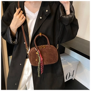 Détail du sac bandoulière en daim marron avec pendentif clé dorée et pompon tissé