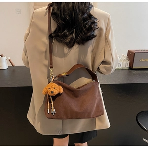 Deep brown suede crescent bag with plush puppy charm worn over a beige blazer
