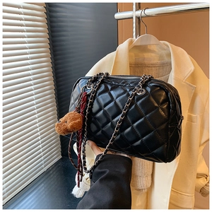 Detail of black quilted shoulder bag with metal chain strap and cute brown bear charm