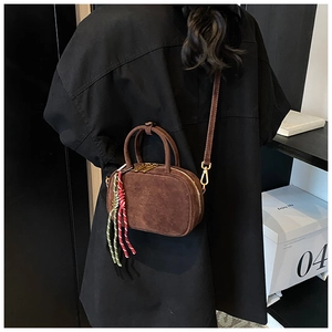 Détail du sac bowling en daim marron avec pompon tricolore et boucles métalliques dorées