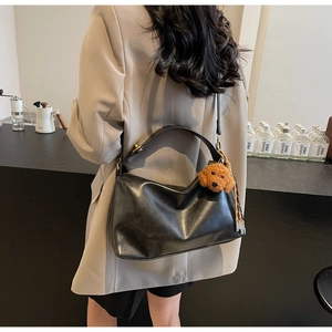 Close-up of black hobo bag in soft leather with a cute brown teddy dog charm on a beige blazer