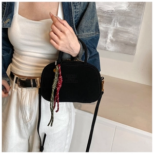 Détail du sac bandoulière noir mat avec logo embossé et breloque tissée bicolore