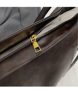 Macro shot of smooth gold metal zipper pull and herringbone lining on dark brown bag