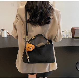 Detail of black suede tote bag with brown teddy dog plush pendant and smooth leather straps